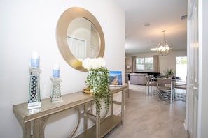 Un salon moderne avec une console, un grand miroir et un coin repas agrémenté d’un lustre.