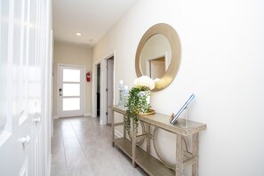 Un couloir avec une porte, un extincteur, une console surmontée d’un miroir et une plante en pot.