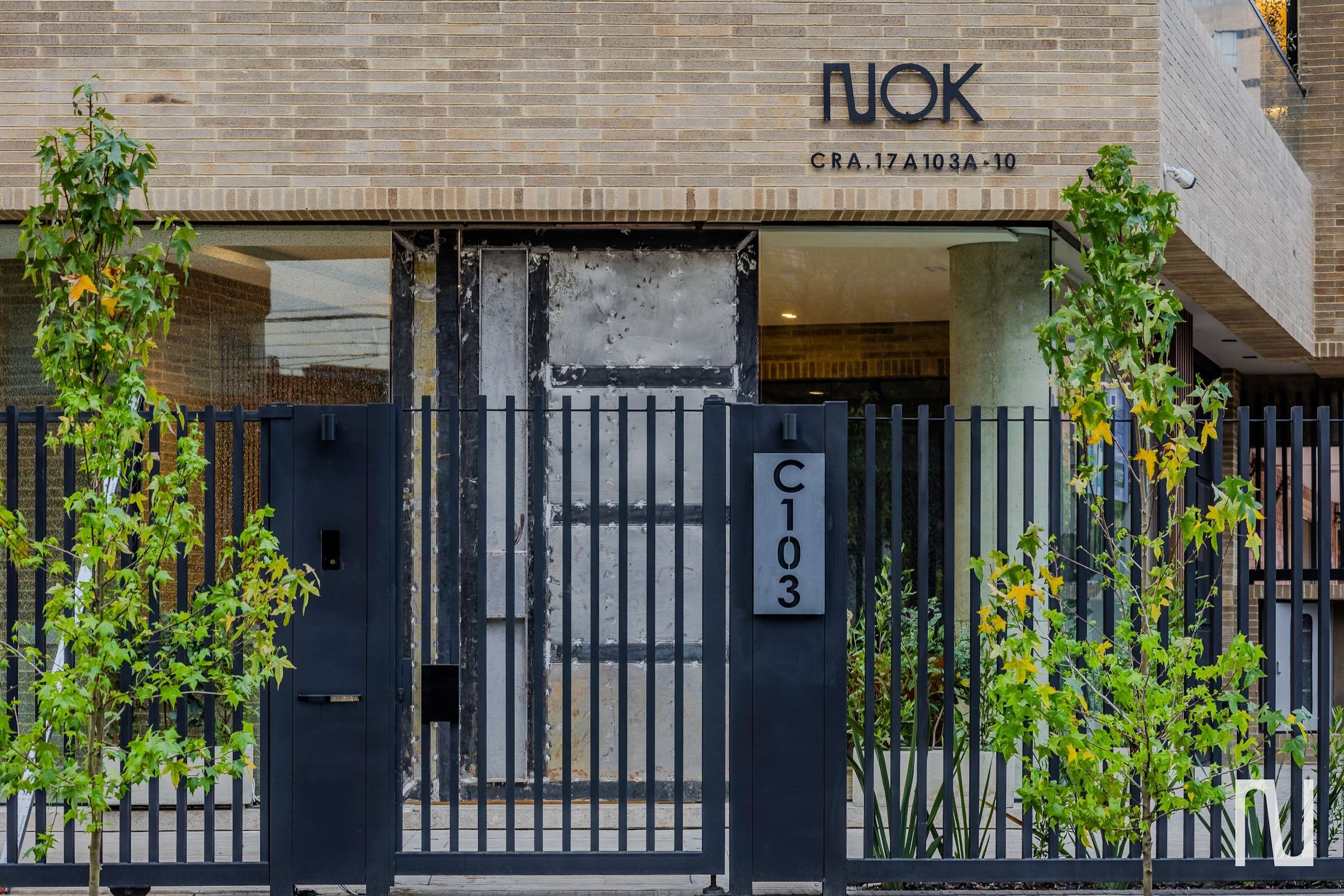 Una entrada de edificio con una reja negra, un cartel de dirección visible y un frente de ladrillo.