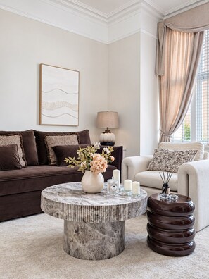 A living room with a round coffee table, a sofa, a lamp, and a window with curtains. - Luxury 6-bed House in Manchester - Free Parking (Manchester)
