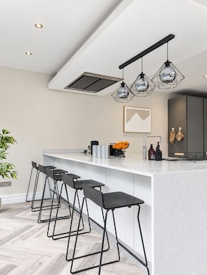 A modern kitchen with a central island, bar stools, pendant lighting, and a visible ceiling vent. - Luxury 6-bed House in Manchester - Free Parking (Manchester)