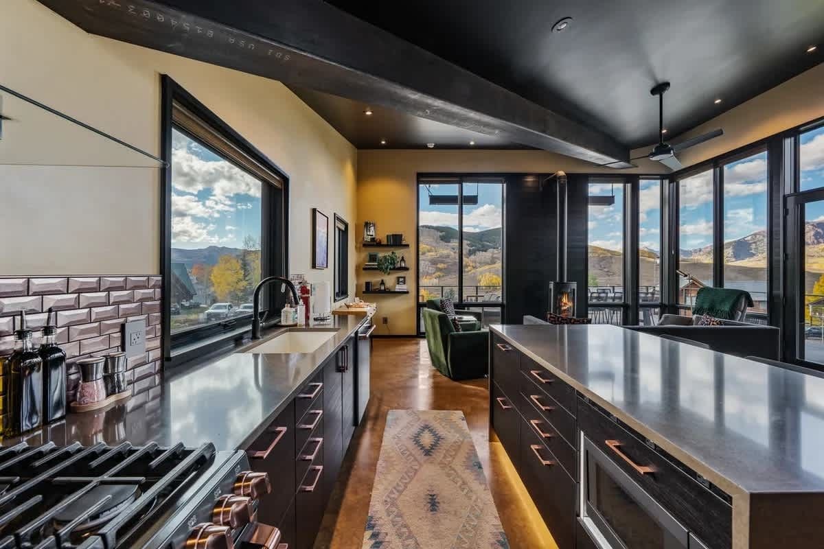 A modern kitchen with large windows, a central island, and a view of the outdoors.