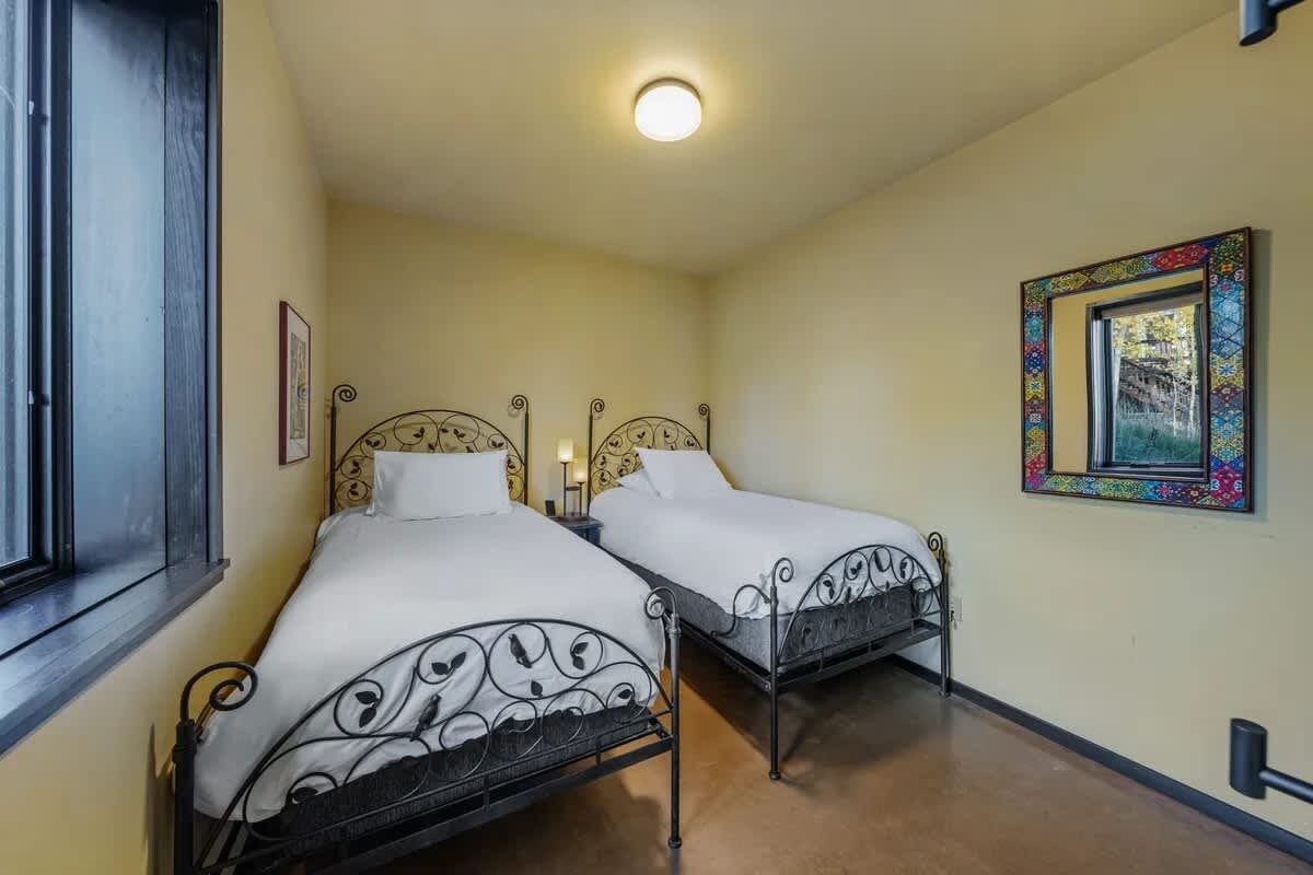Una habitación con dos camas, una ventana, una lámpara en el techo y un cuadro en la pared.