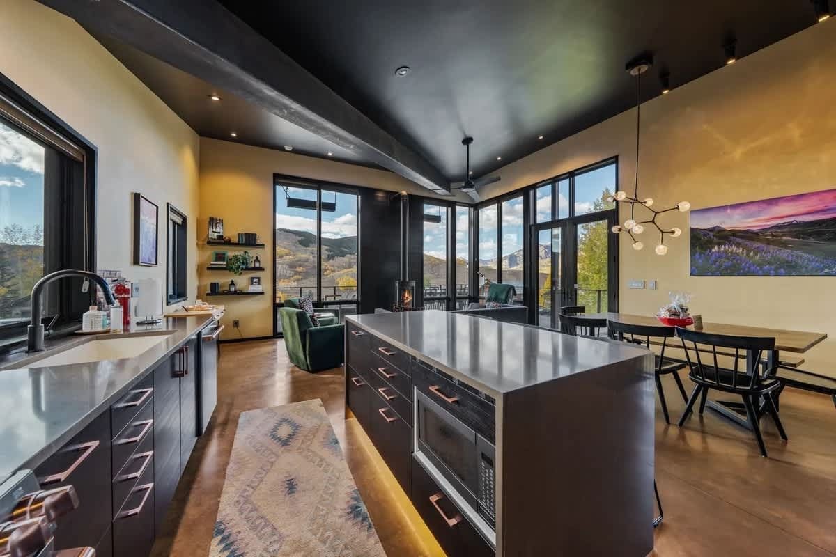 A modern kitchen with a large island, built-in appliances, and a dining area with a view of the outdoors.