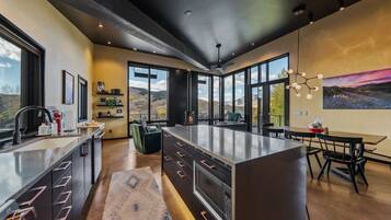 A modern kitchen with a large island, built-in appliances, and a dining area with a view of the outdoors.