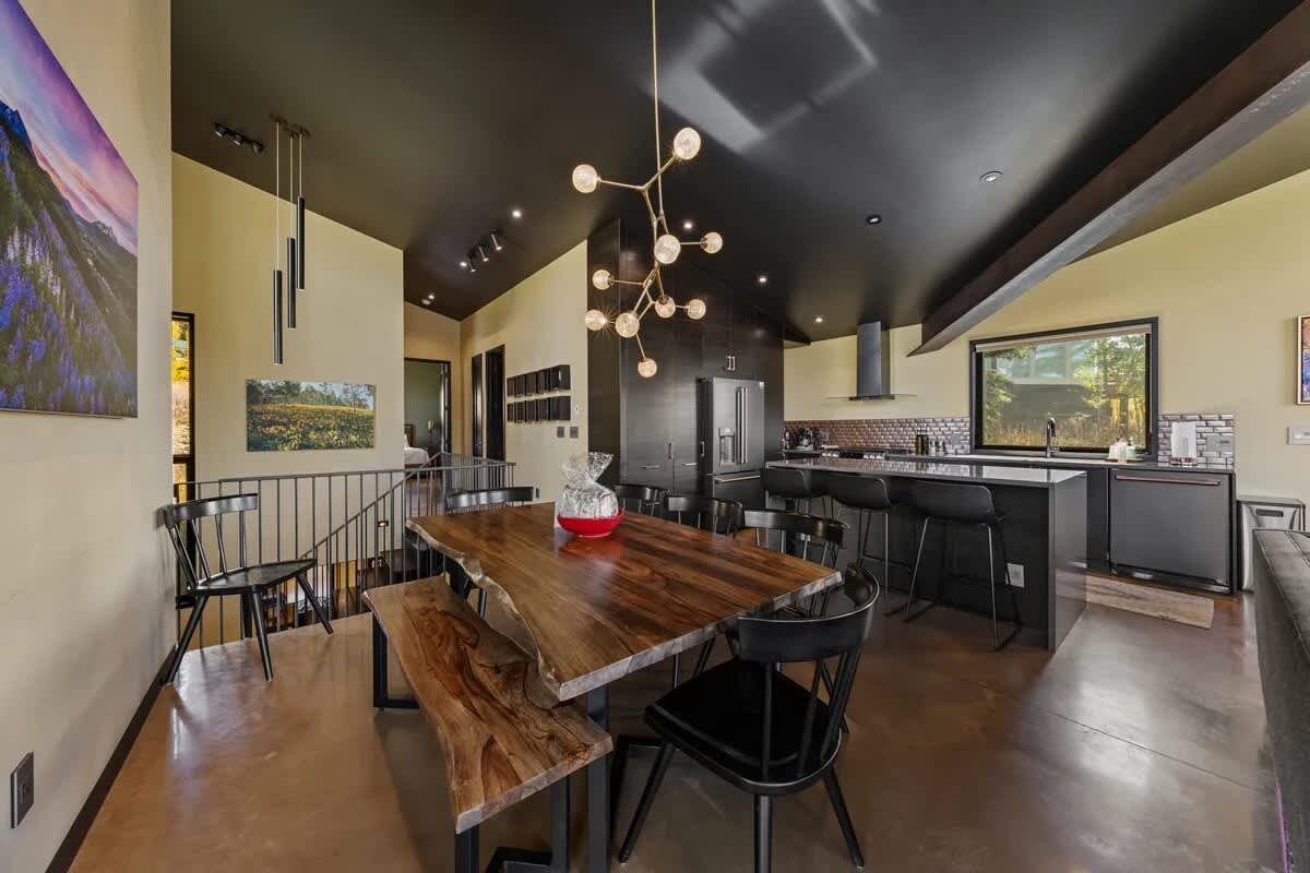 Una cocina moderna con una isla central, iluminación colgante y un comedor con mesa y sillas de madera.