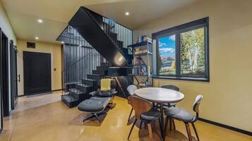 Un interior moderno con una escalera, un comedor con mesa y sillas redondas, y una estantería.
