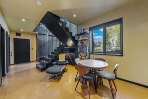 A modern interior with a staircase, a dining area with a round table and chairs, and a bookshelf. - Mountain Escape - Hot Tub - Views - Firepit (Crested Butte)