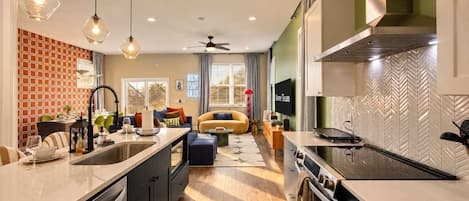 A modern kitchen with a central island, built-in oven, and a dining area with a sofa and table.