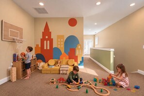Ein Kinderspielzimmer mit einem Basketballkorb, einer farbenfrohen Stadtsicht-Mural und verschiedenen Spielsachen und Spielgeräten.