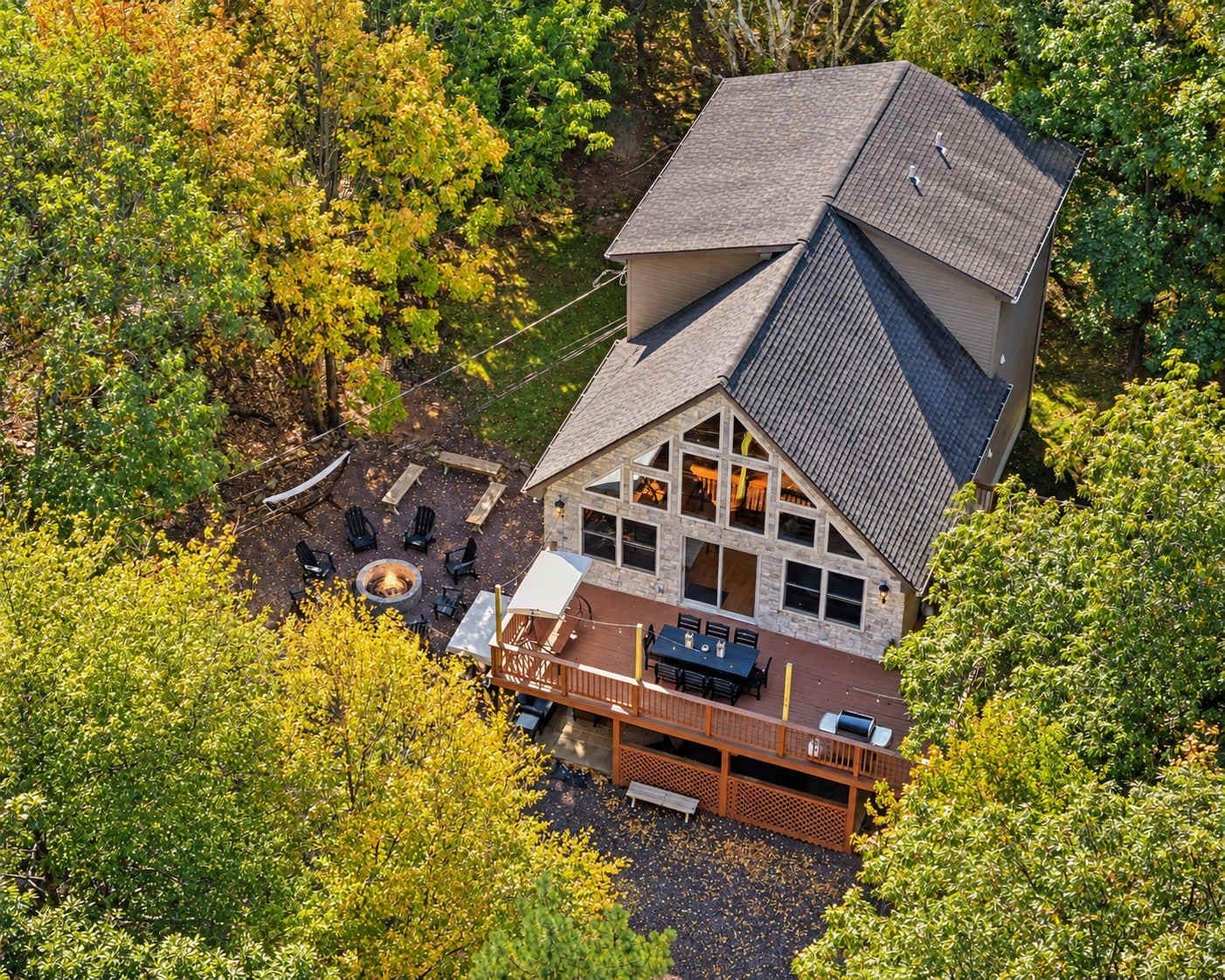 A house with a large deck, a fire pit, and a view of the surrounding forest.