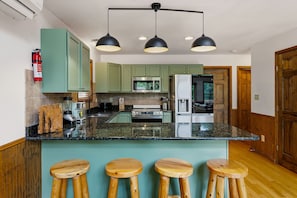 A kitchen with green cabinets, a central island with stools, a microwave, a refrigerator, and a fire extinguisher. - Poconos Retreat Sauna Hot Tub Fire Pit Games (Lake Harmony)