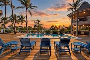 A wooden deck with lounge chairs and a swimming pool, surrounded by palm trees and a sunset view. - Private Island Oasis Pool Dock Boat-in Only (Longboat Key)