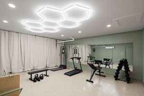 Ein Fitnessraum mit Trainingsgeräten, einem Spiegel und einer sechseckigen Deckenleuchte.