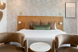 A hotel room with a bed, two bedside lamps, a rattan headboard, and a patterned wallpaper. - Lakin It Easy Luxe Waterfront Oasis Sleeps 16 (Mesa)