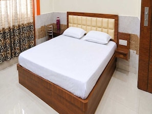 A neatly made bed with a wooden frame and white bedding in a hotel room. - Classic Hotel DI Regency (Bathinda)