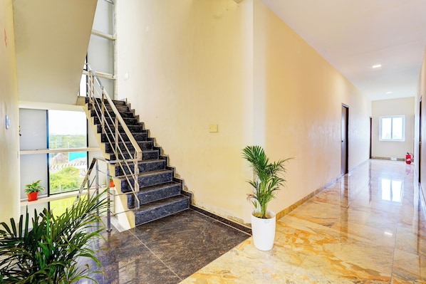 A spacious hallway with a marble floor, a staircase with black steps, and a potted plant.