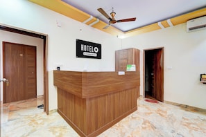 A hotel reception desk with a 'HOTEL' sign, a ceiling fan, and a reception area.