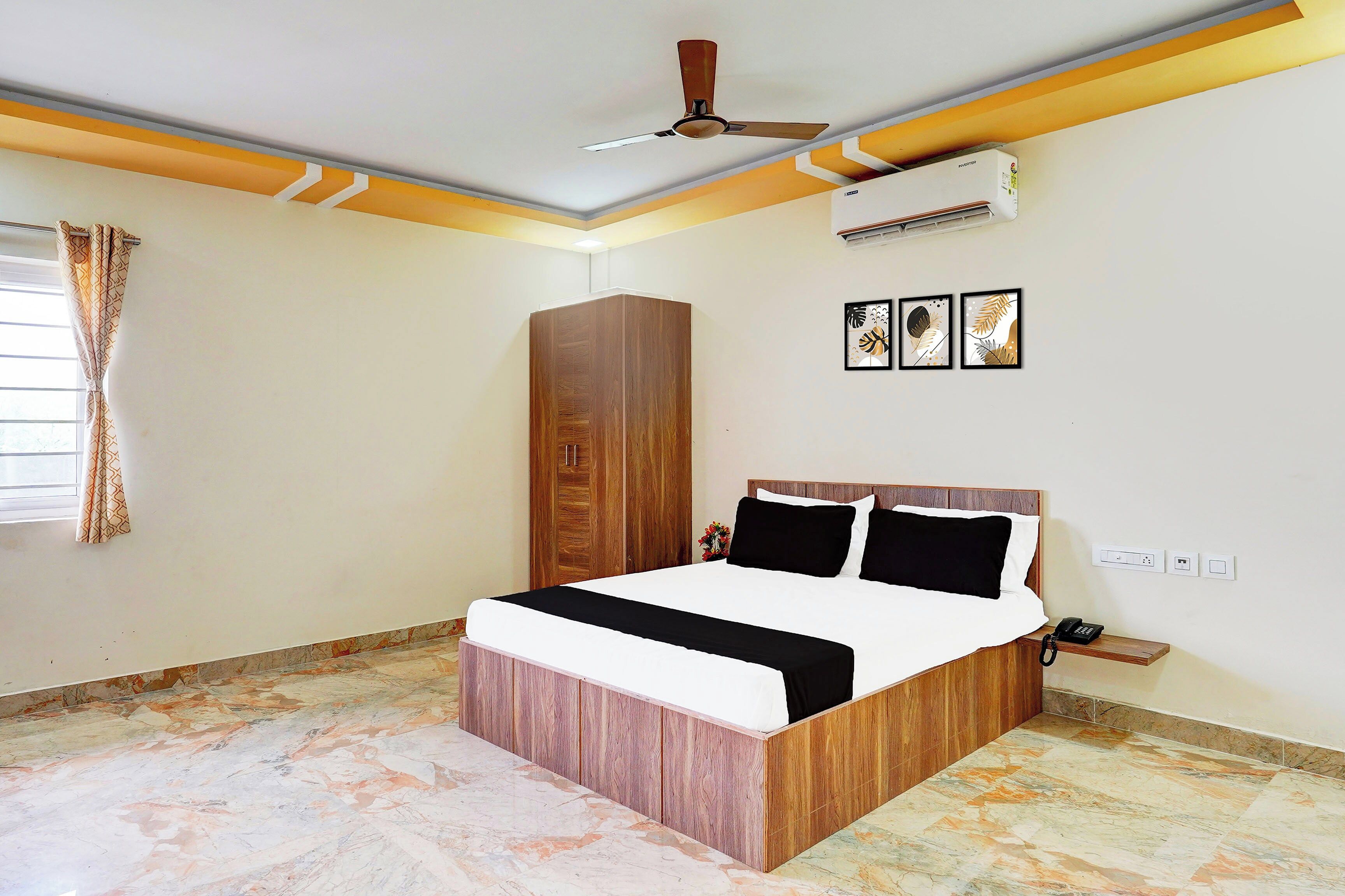 A hotel room with a bed, wardrobe, ceiling fan, air conditioning unit, artwork, and a telephone.