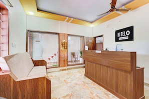 A hotel reception area with a wooden reception desk, a seating area with a sofa, and a ceiling fan. - Hotel O Sriperambadhur (Sriperumbudur)
