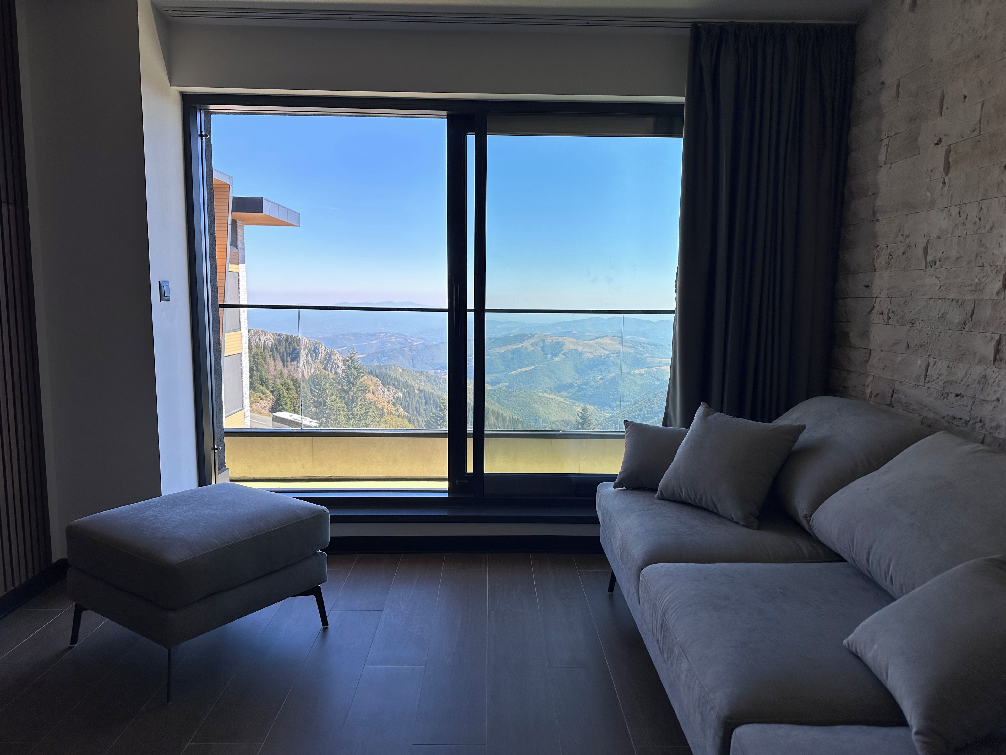 A modern living room with a large window, a sofa, and an ottoman.