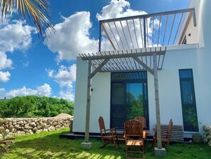 A modern house with a patio, wooden chairs, and a stone wall. - Dhow Flat at Paje Beach | Step from your Garden into the Pool (Paje)