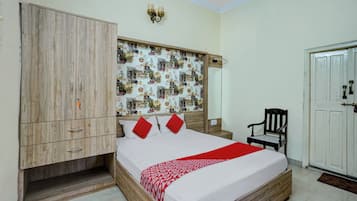 A bedroom with a wooden wardrobe, a bed with red pillows, a chair, and a wall with a cityscape mural.