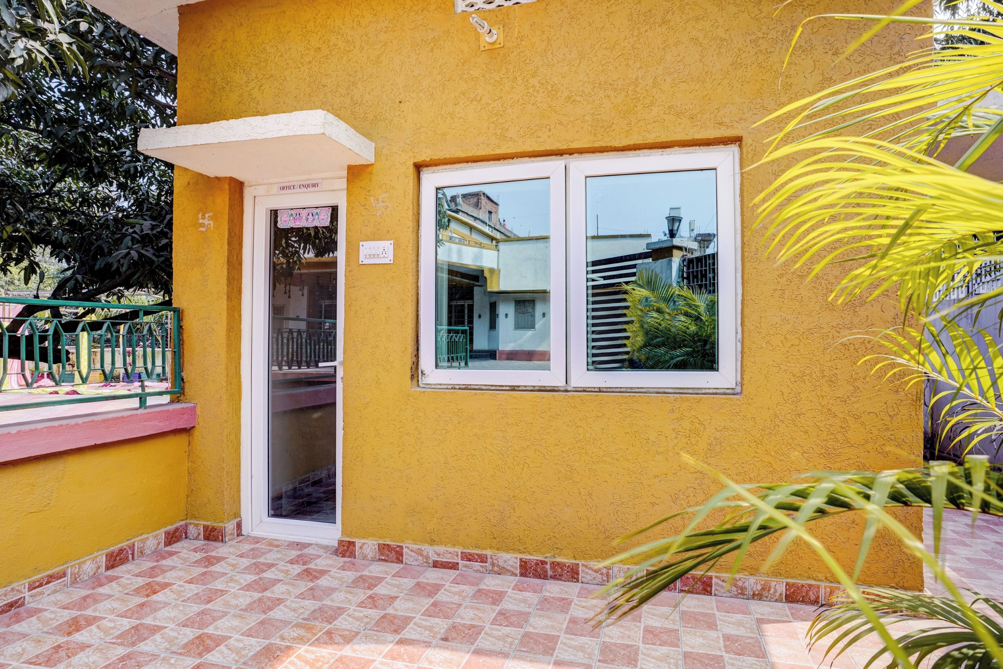 Un edificio amarillo con un patio empedrado, una puerta con la leyenda 'Office/Enquiry' y una ventana que da a un edificio vecino.