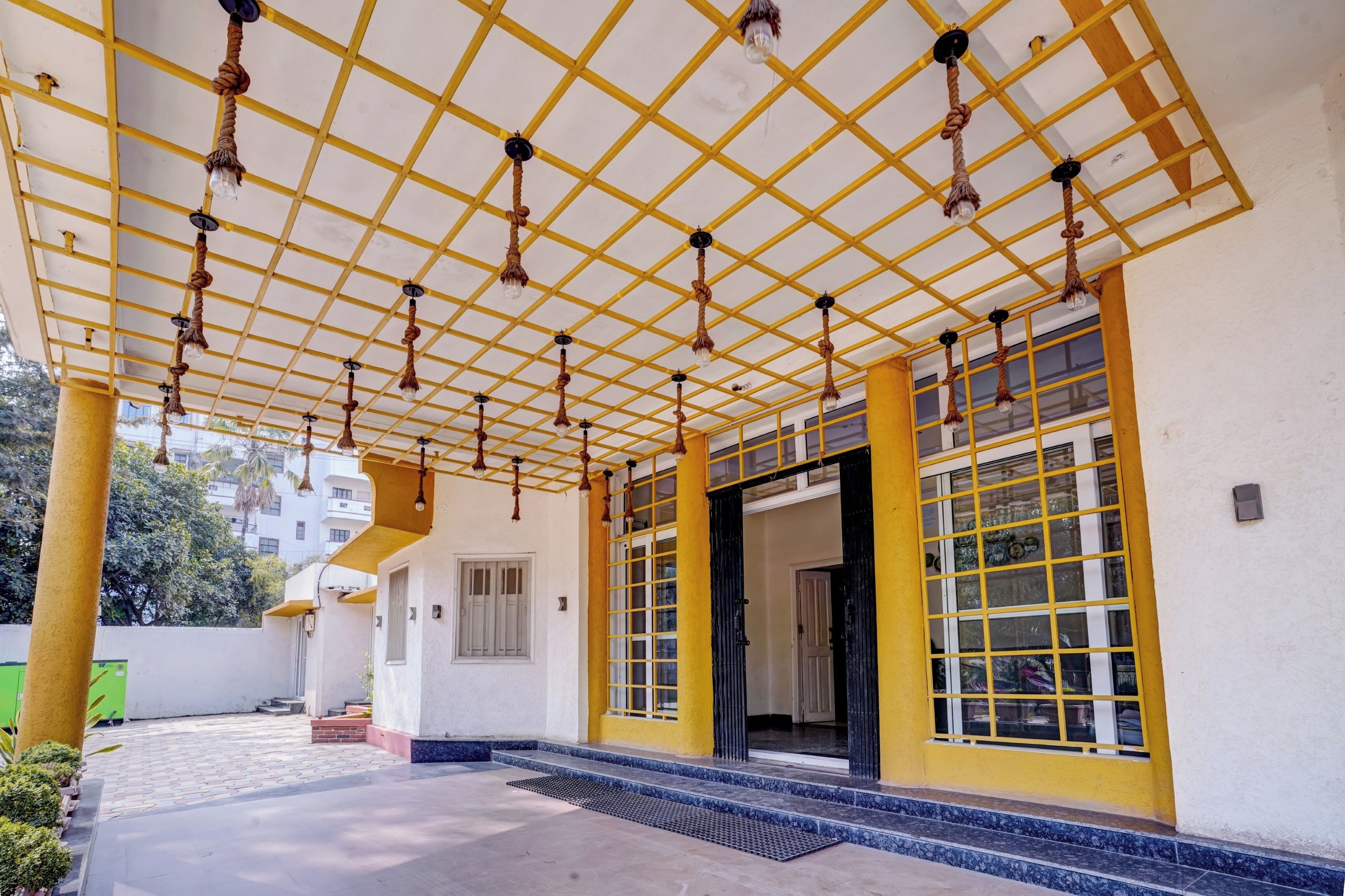 A covered outdoor area with a yellow grid ceiling, a set of stairs leading to a door, and a view of a building in the background.
