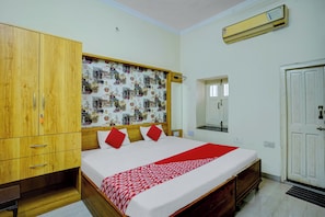 Ein Schlafzimmer mit einem hölzernen Kleiderschrank, einem Bett mit rot-weißer Bettwäsche, einer gemusterten Wand und einer weißen Tür.