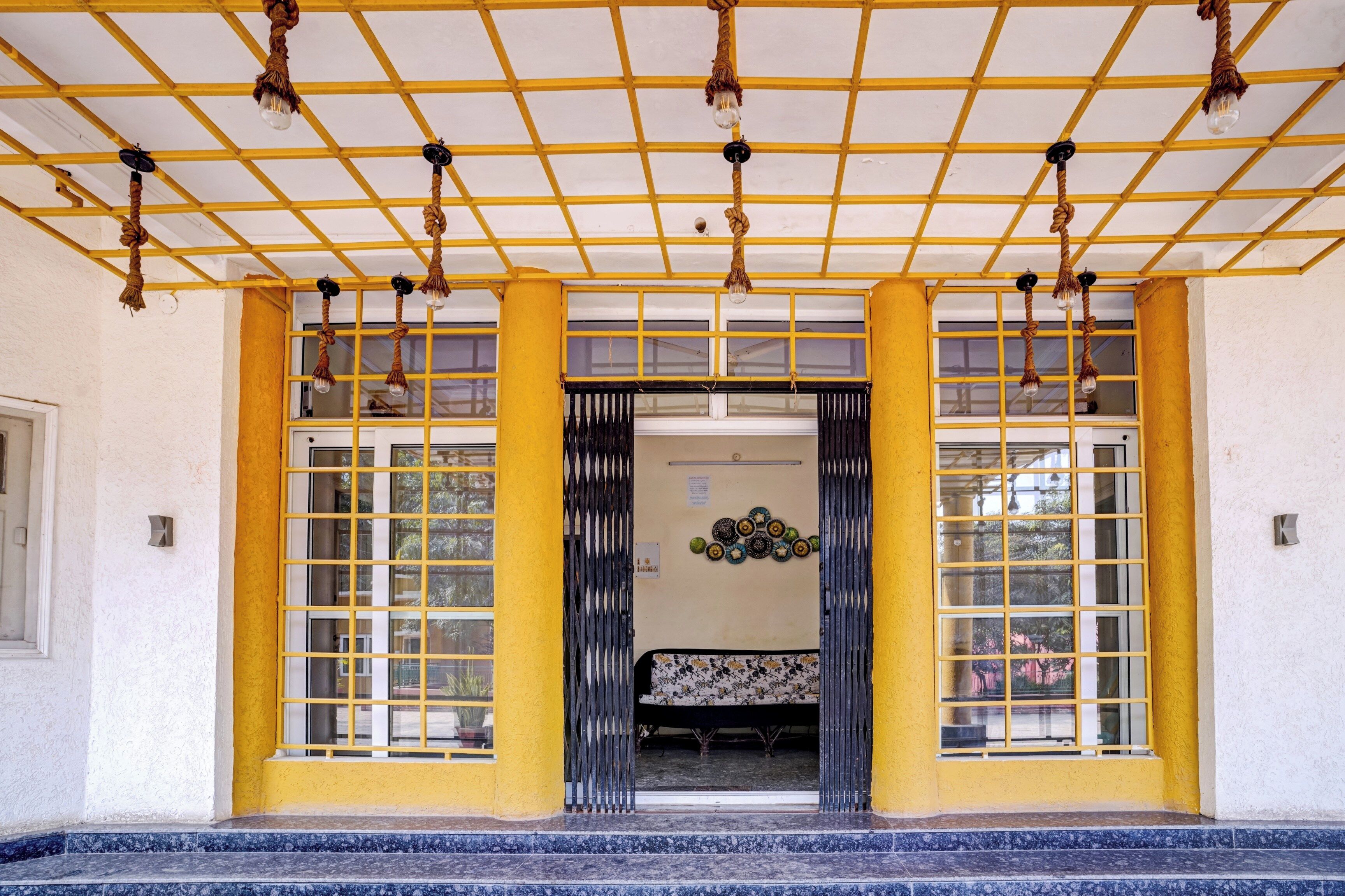 Fachada de edificio con una decoración amarillo y blanco, destacando un techo tipo celosía y varias lámparas colgantes.