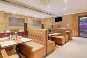 A hotel restaurant with booth seating, a flat-screen TV, and a modern chandelier. - Townhouse Arcot Road Near Kauvery (Chennai)