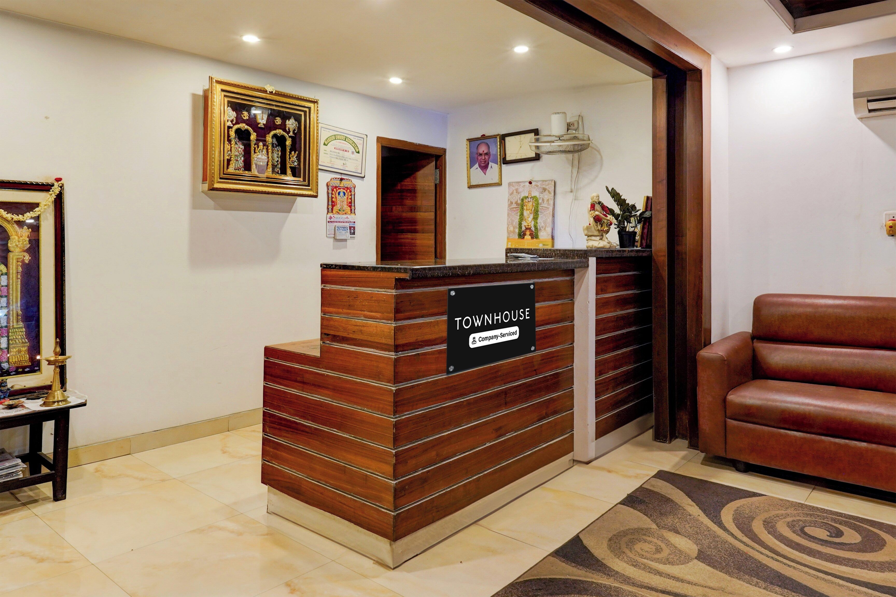 Una mesa de recepción con un cartel que indica servicio de la empresa, un certificado enmarcado en la pared y una butaca de cuero rojo a la derecha.