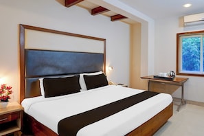 A hotel room with a large bed, bedside table, and a window with a view of greenery. - Townhouse Arcot Road Near Kauvery (Chennai)