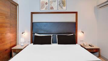 A hotel room with a large bed, two bedside tables, a wooden wardrobe, and three framed artworks on the wall.