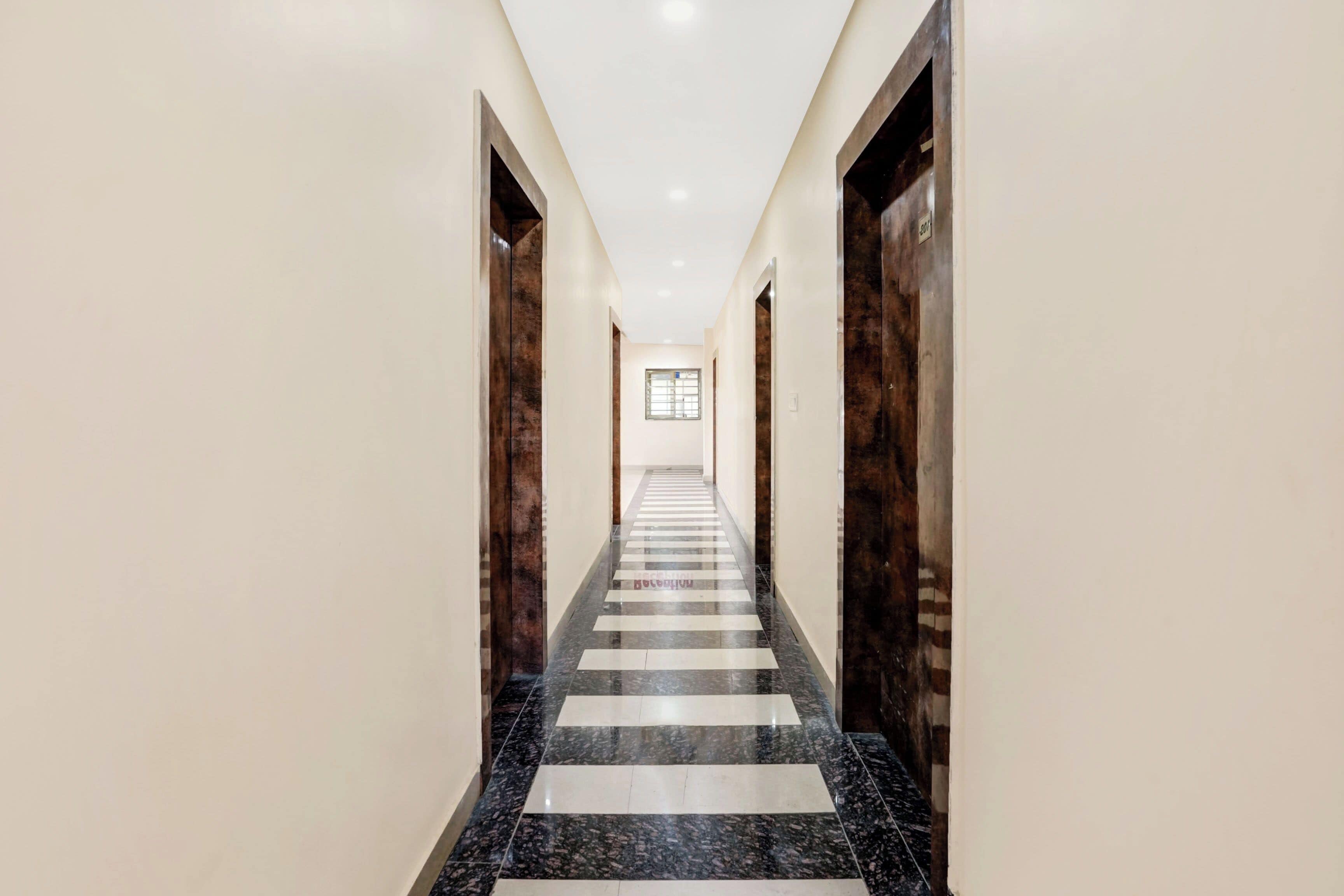 A long, narrow hallway with a checkered floor pattern, flanked by walls with a wooden finish and a door at the end.