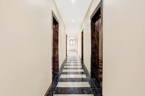Un largo y estrecho pasillo con piso a cuadros, flanqueado por paredes de madera y una puerta al final.