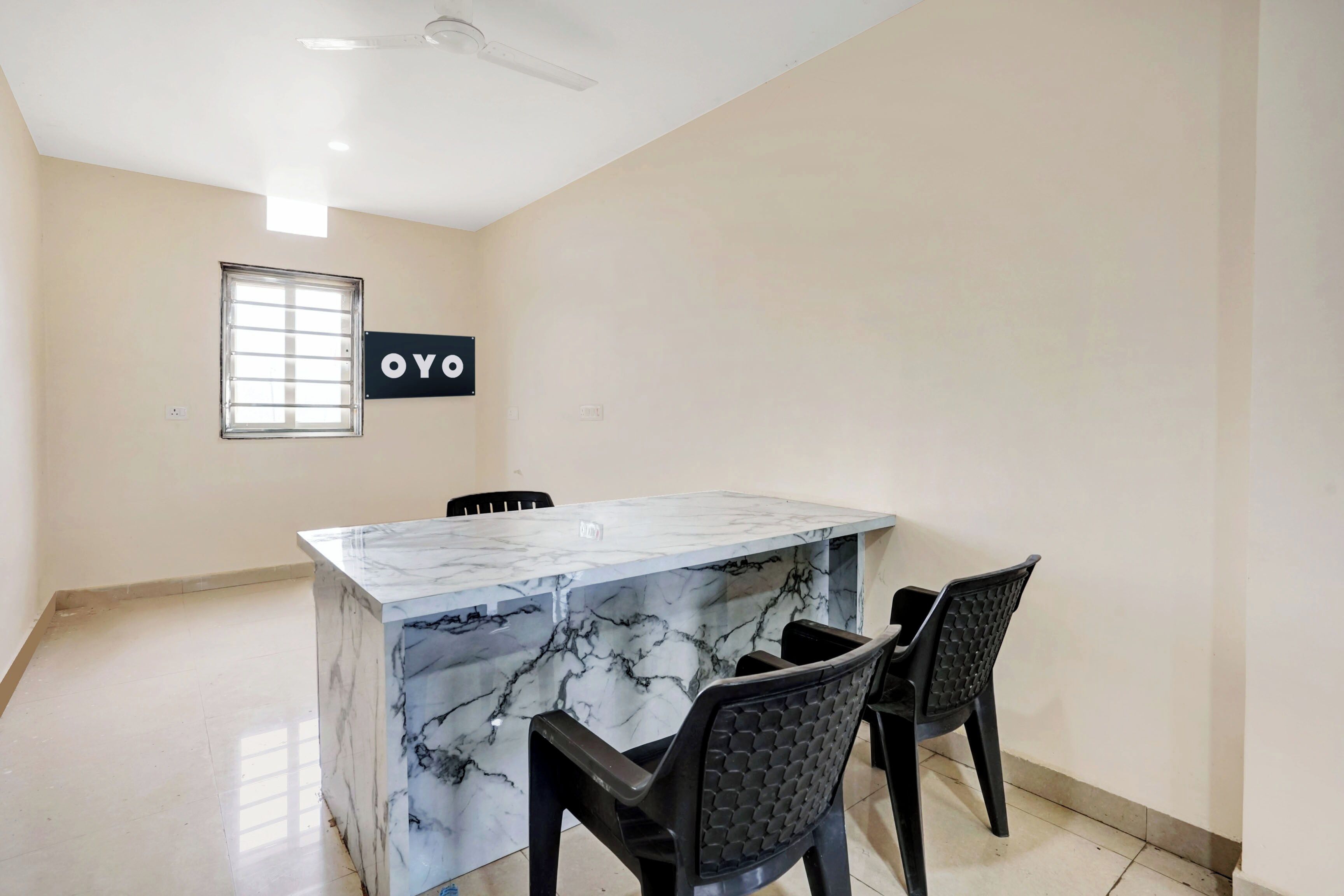 A room with a marble island, two chairs, a ceiling fan, a window with blinds, and a sign with 'OYO' on the wall.