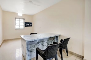 A room with a marble island, two chairs, a ceiling fan, a window with blinds, and a sign with 'OYO' on the wall. - Hotel O SWEDHA HOTEL (Hazaribagh)