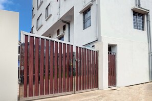 Una entrada protegida por un portón a un edificio con fachada blanca y varias ventanas.