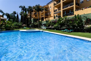 A swimming pool with a clear blue water surface, surrounded by a well-maintained lawn and various tropical plants. - Apartment 'Casa Kapano' with Mountain View, Wi-Fi and Air Conditioning (La Cala de Mijas)
