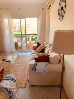 A modern living room with a sofa, a coffee table, and a lamp. There is a balcony with a view of the outside. - Apartment 'Casa Kapano' with Mountain View, Wi-Fi and Air Conditioning (La Cala de Mijas)