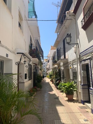 A narrow street with buildings on either side, featuring balconies with plants, a clear sky, and a paved path. - Apartment 'Casa Kapano' with Mountain View, Wi-Fi and Air Conditioning (La Cala de Mijas)