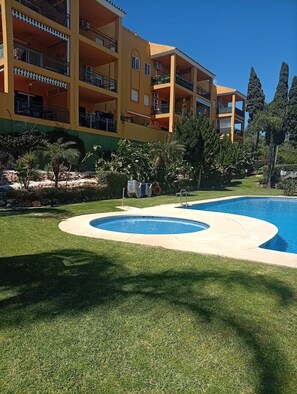 A hotel with a swimming pool, green lawn, and a multi-story building with balconies. - Apartment 'Casa Kapano' with Mountain View, Wi-Fi and Air Conditioning (La Cala de Mijas)