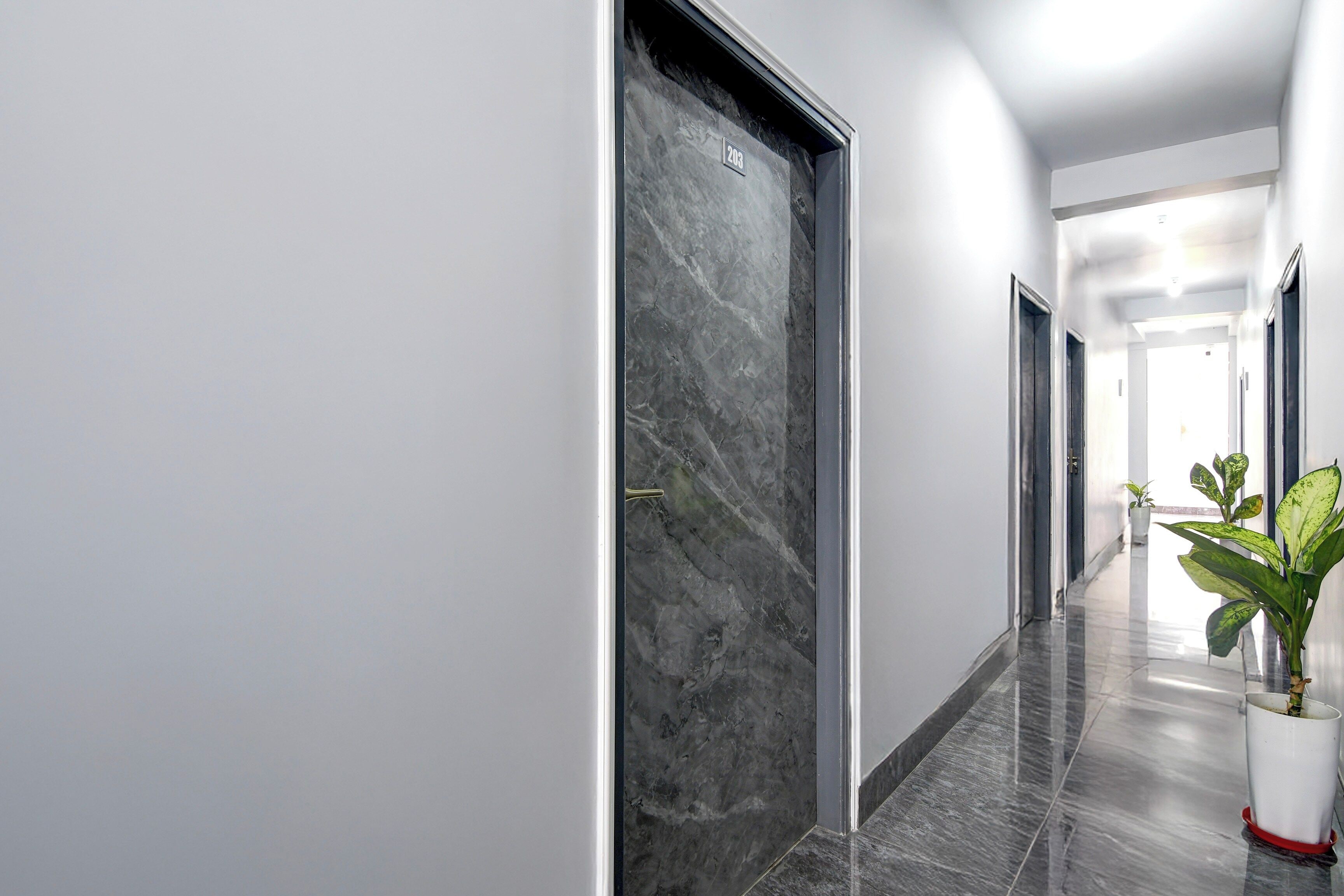 Un pasillo moderno con piso de mármol, una planta en maceta y una puerta con placa numérica.