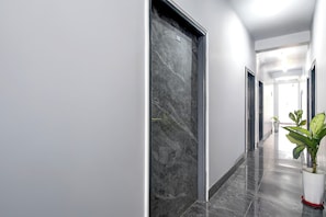 Un pasillo moderno con piso de mármol, una planta en maceta y una puerta con placa numérica.