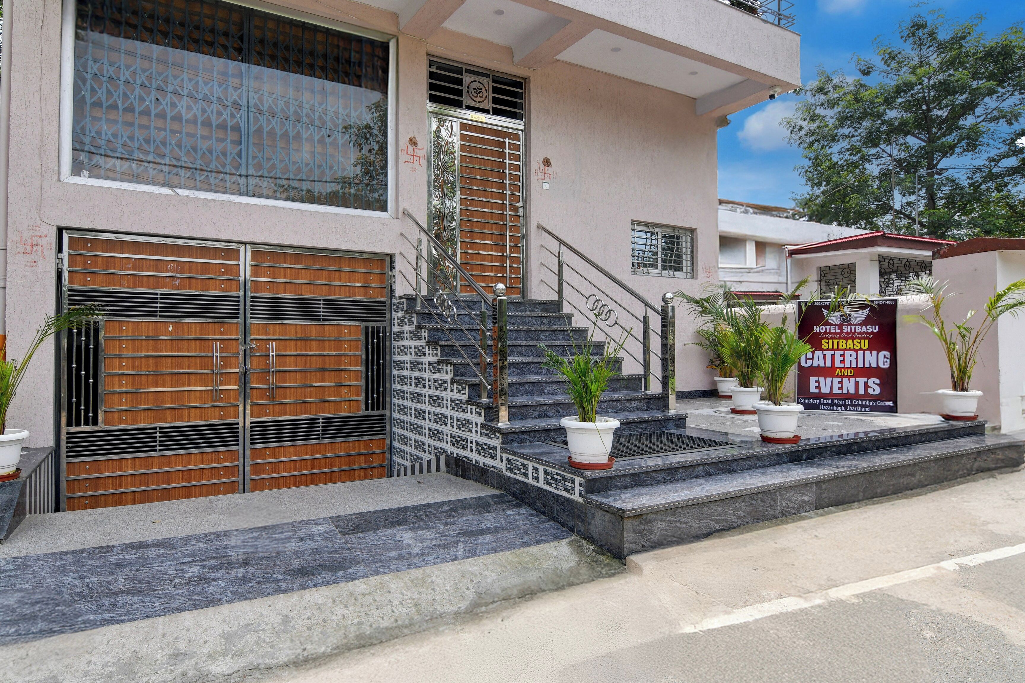 Entrada de un hotel con un camino de acceso porticado, una escalera y un cartel publicitario de servicios de catering y eventos.