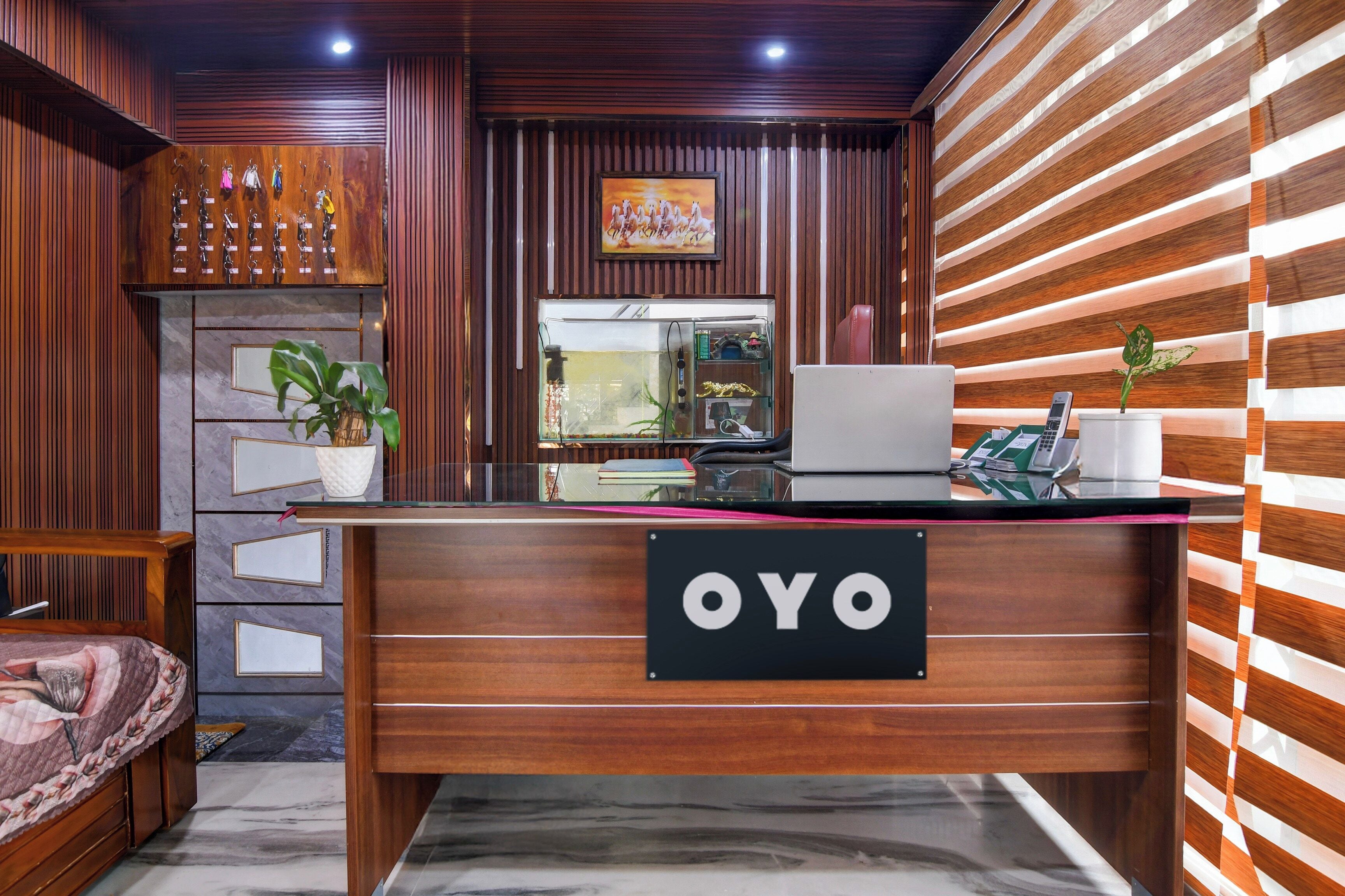 A reception desk with a sign reading 'OYO,' a potted plant, a laptop, and a telephone.