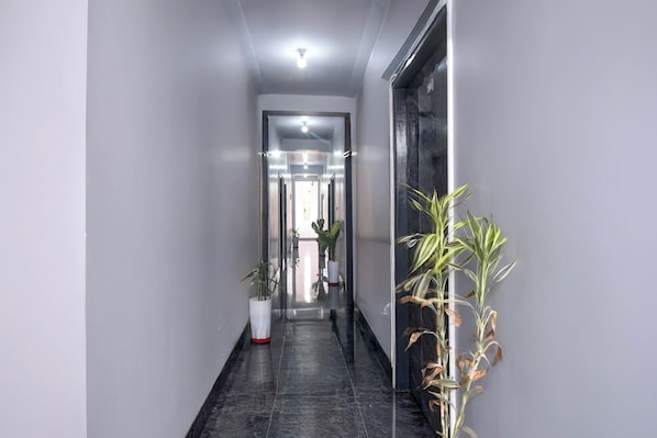 Un pasillo con una puerta de cristal que da a una habitación, una planta en maceta a la izquierda y otra a la derecha.