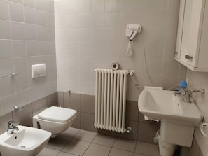 Un baño con inodoro, bidé, lavamanos y un teléfono fijo en la pared.